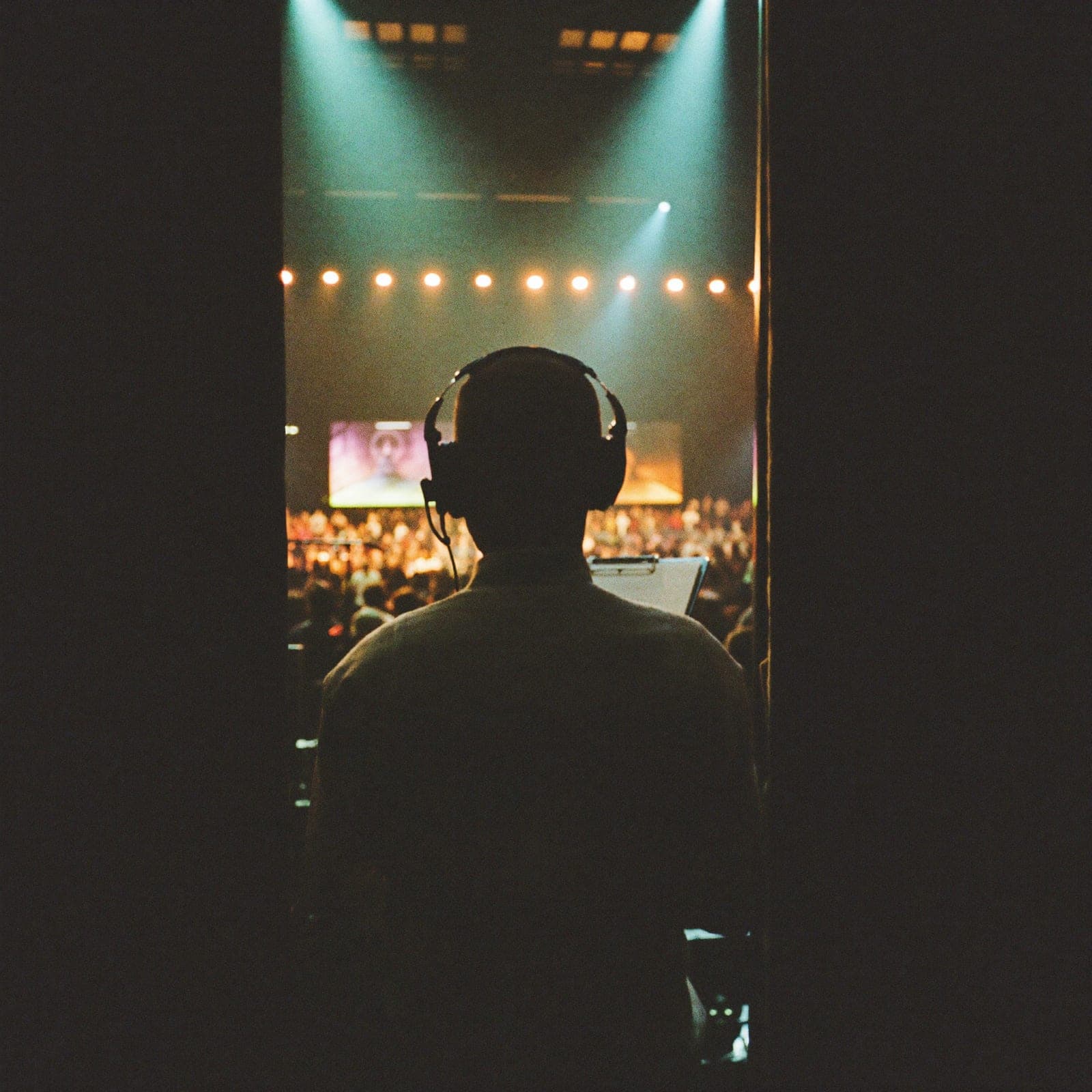 Show caller with a headset and clipboard watching a full event room from backstage